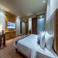 A hotel room with a wooden accent wall, a bed with white bedding, a television mounted on the wall, and a sliding door closet.