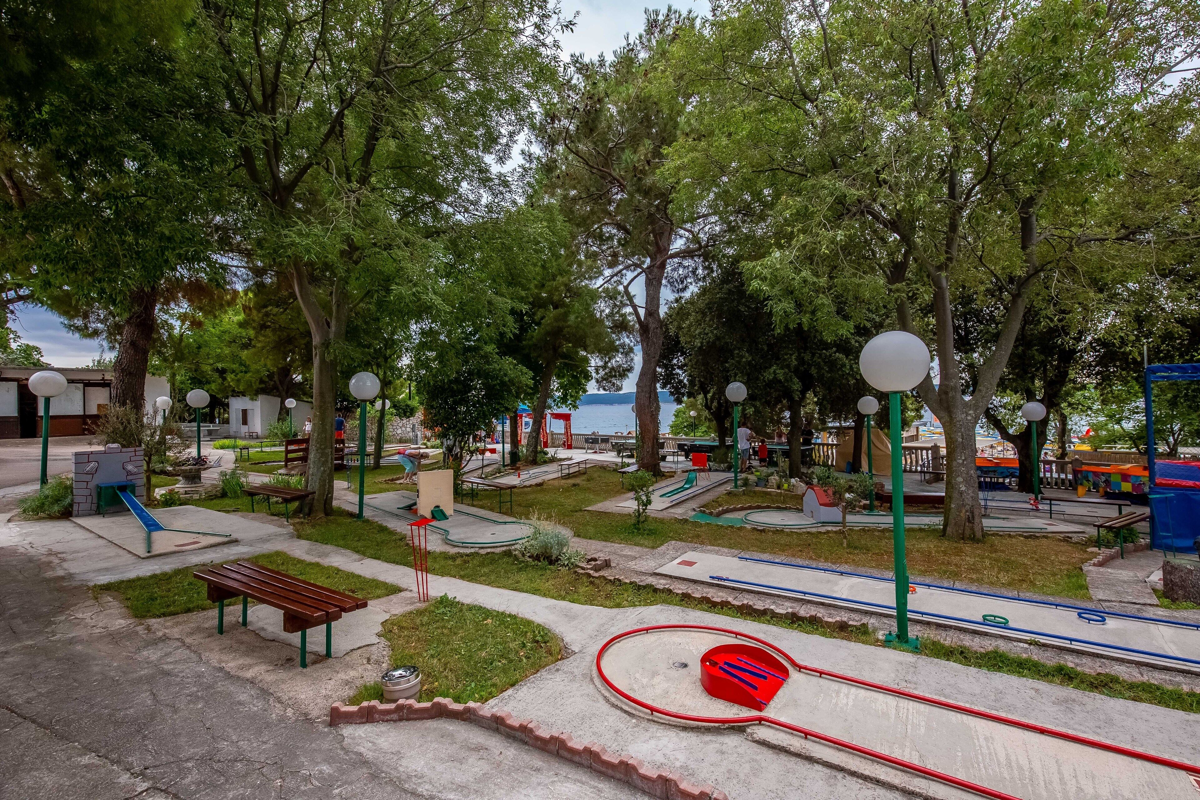 Un parque con juegos infantiles, bancos y una masa de agua al fondo.
