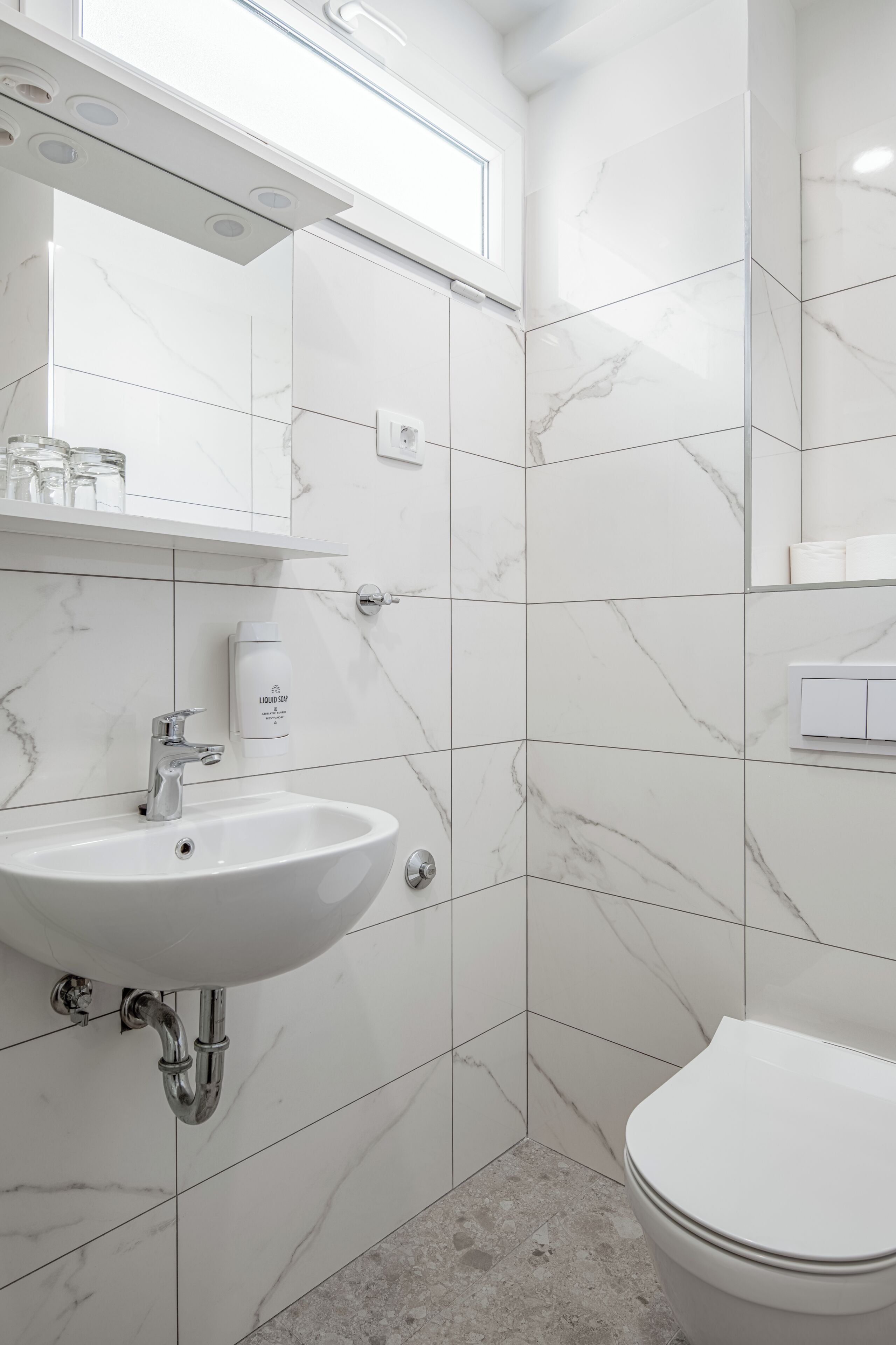 A bathroom with a white sink, mirror, and toilet, all set in a room with white marble tiles.