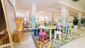 A brightly lit indoor space with a large easel, colorful stools, and a table with toys. - Annex Slaven (Crikvenica)