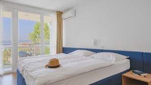 A hotel room with a large bed, a nightstand, an air conditioning unit, and a view of the outdoors. - Annex Slaven (Crikvenica)