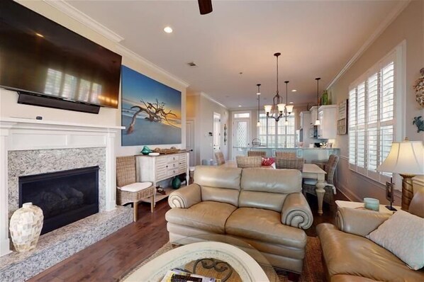 A spacious living room with a fireplace, leather sofa, and a large flat-screen TV mounted above it. - Ocean Cottage 36 - Sweet Retreat 6-Seater Cart The Cottages at Jekyll Island (Jekyll Island)