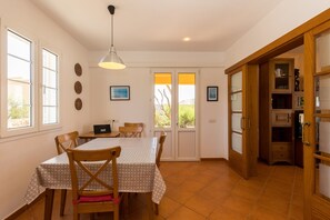 A dining area with a table, chairs, a hanging light, and a view through a door.