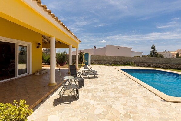 A covered outdoor area with a pool, stone flooring, and outdoor furniture.