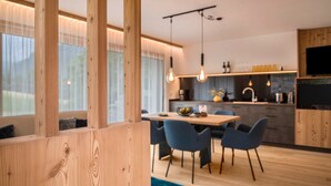 A modern kitchen with wooden cabinetry, a dining area with blue chairs, and pendant lighting. - Apartment 'Lara Siela' with Mountain View, Private Terrace and Wi-Fi (St. Ulrich)