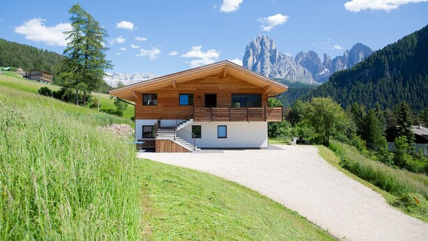 A modern two-story wooden house with a gravel driveway, surrounded by lush greenery and mountains. - Apartment 'Lara Siela' with Mountain View, Private Terrace and Wi-Fi (St. Ulrich)