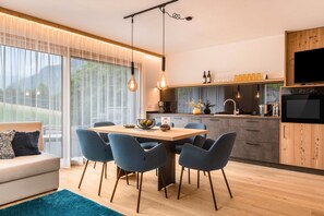 A modern kitchen with a dining area, large windows, and a TV.
