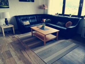 A living room with a black leather sofa, a wooden coffee table, a striped rug, and a small side table with a lamp. - Dreimal Seeblick - Ferienwohnung Paul (Edertal)