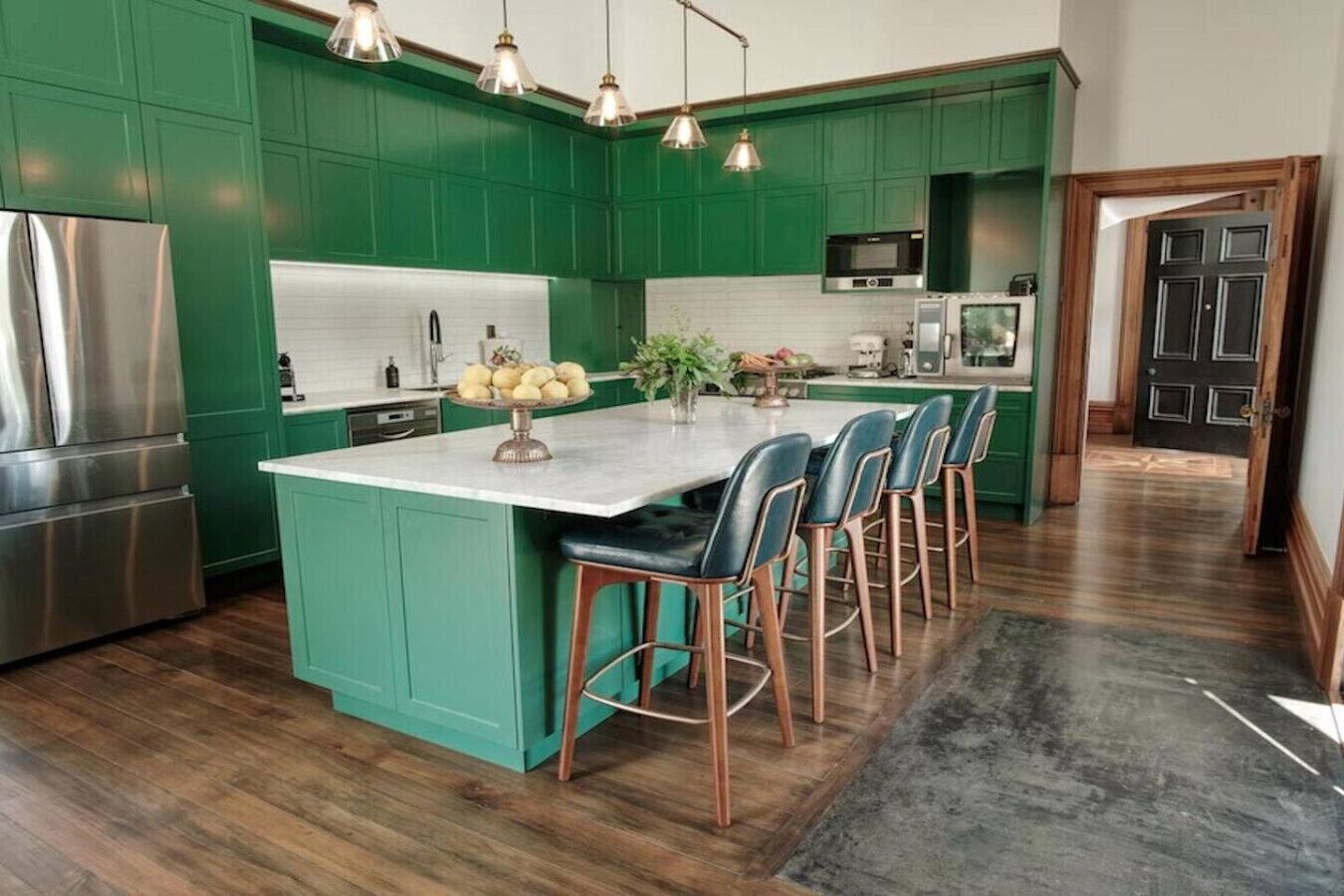 Une cuisine avec des meubles de couleur verte, un réfrigérateur en acier inoxydable, un four à micro-ondes et un grand îlot central doté de tabourets de bar.