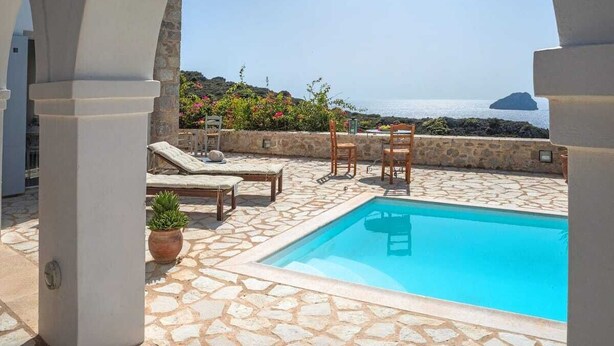 A pool area with stone flooring, lounge chairs, and a view of the sea. - Fiora Paradise Villa Resort (kythira)