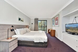 A modern hotel room with a large bed, a desk, a television, and artwork on the walls.