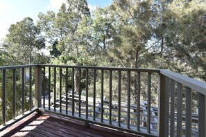 A wooden deck with a railing, overlooking a forested area with various trees.