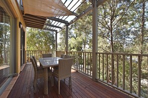 An outdoor deck with a table and chairs, surrounded by a wooden railing, overlooking a forested area.