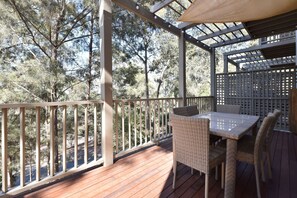 A wooden deck with a table and chairs, surrounded by a wooden railing and trees.