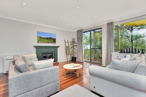 A modern living room with a fireplace, two sofas, a coffee table, and a large window with a view of greenery.