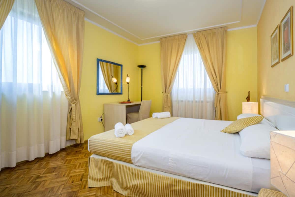 A hotel room with a large bed, a desk, a chair, a lamp, and a mirror.