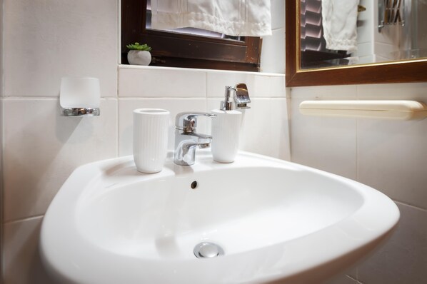 A white bathroom sink with a mirror above it, a towel rack, and a small plant on the shelf.