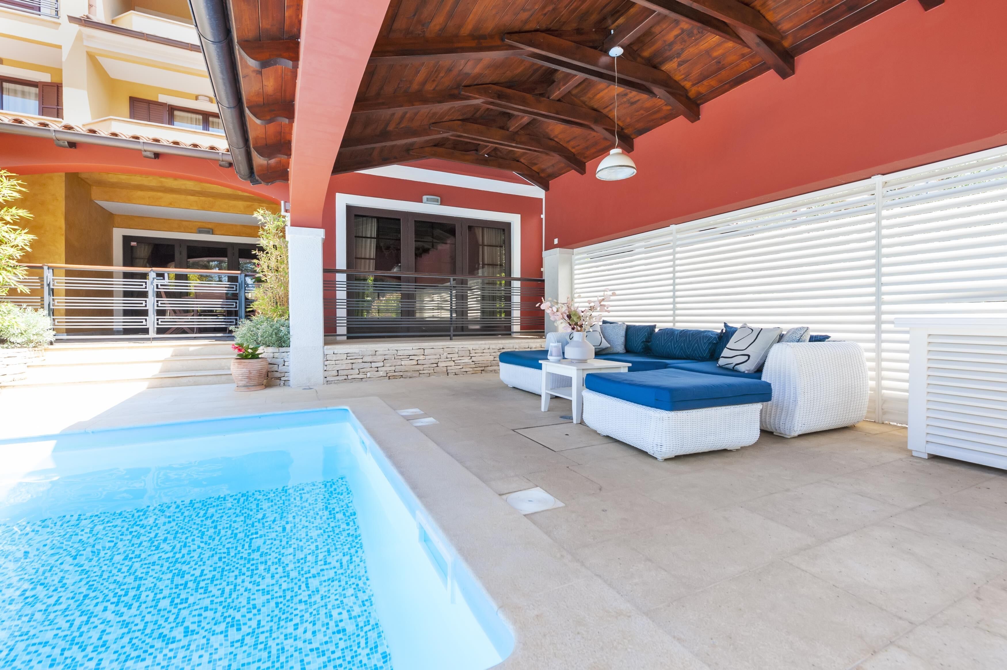 A poolside area with a pool, white wicker furniture, and a red building in the background.