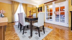 A dining area with a wooden herringbone floor, a dark wooden table, white chairs, and a beige rug. - Apartments with Shared Pool Villa Rossella 1 (Rovinj)