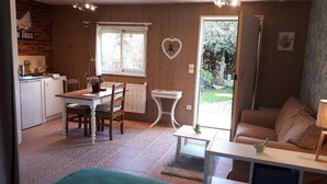 A cozy room with a bed, a dining table with chairs, a small white table, a sofa, and a window with a heart-shaped decoration. - Tara, guest studio in the countryside with kitchenette (Saint Sylvestre de Cormeilles)