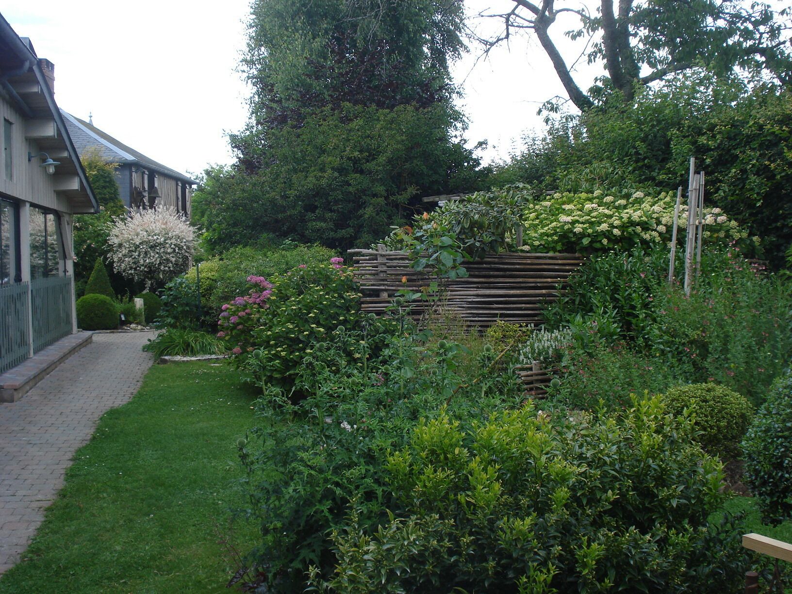 Un jardín con cerda de madera, diversas plantas y un sendero que lleva a un edificio.