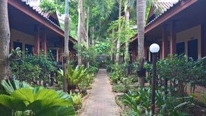 A pathway flanked by lush greenery and traditional architecture, leading to a building with multiple doors. - Penny Bangalow Resort (Ko Chang)