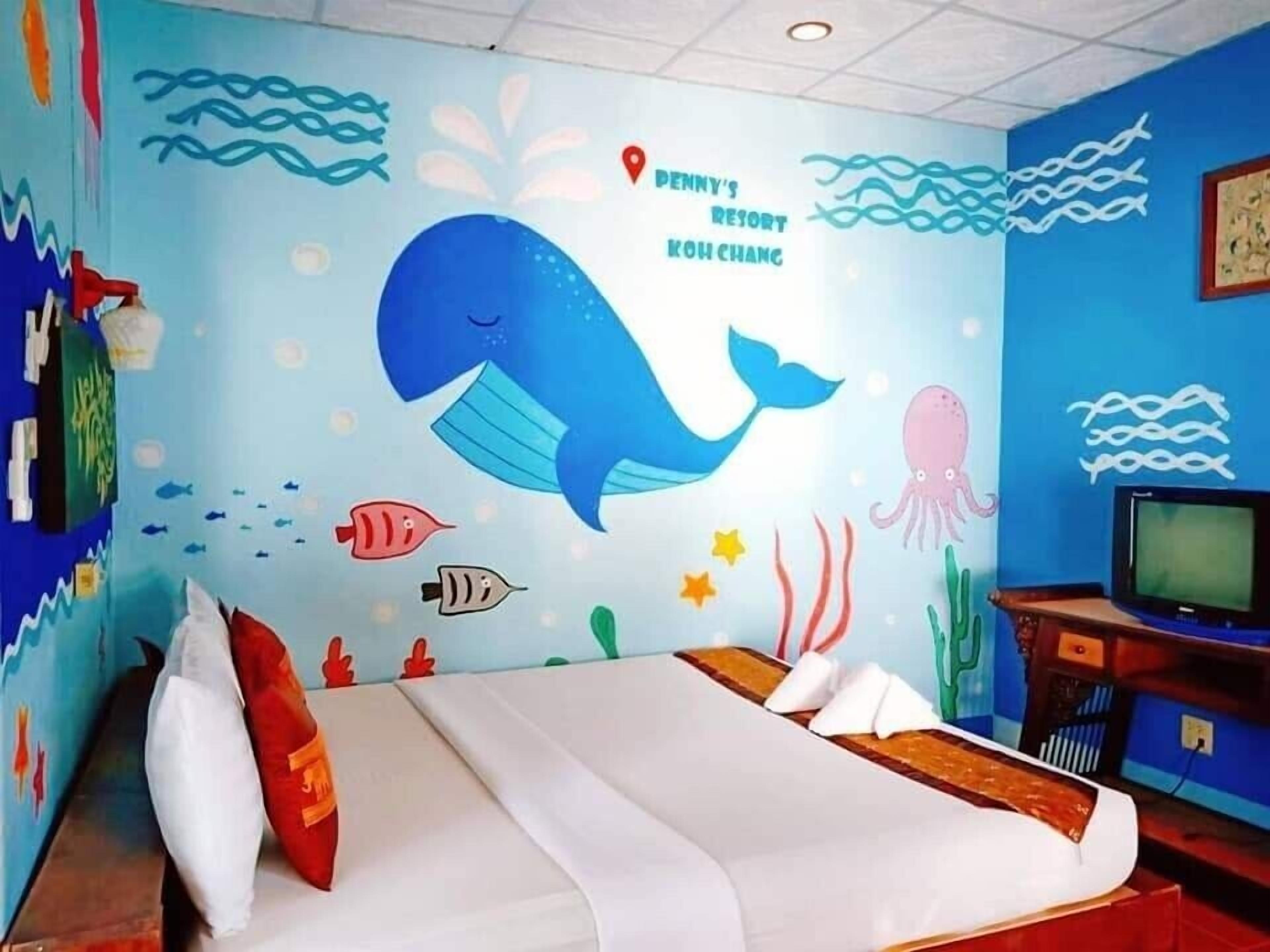 A room with a bed, a television, and a wall decorated with an underwater theme including a whale, fish, and seaweed.