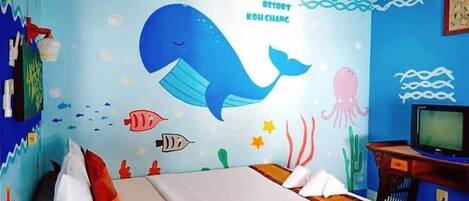 A room with a bed, a television, and a wall decorated with an underwater theme including a whale, fish, and seaweed.