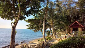 A beachside setting with a small building, outdoor seating, and palm trees. - Penny Bangalow Resort (Ko Chang)