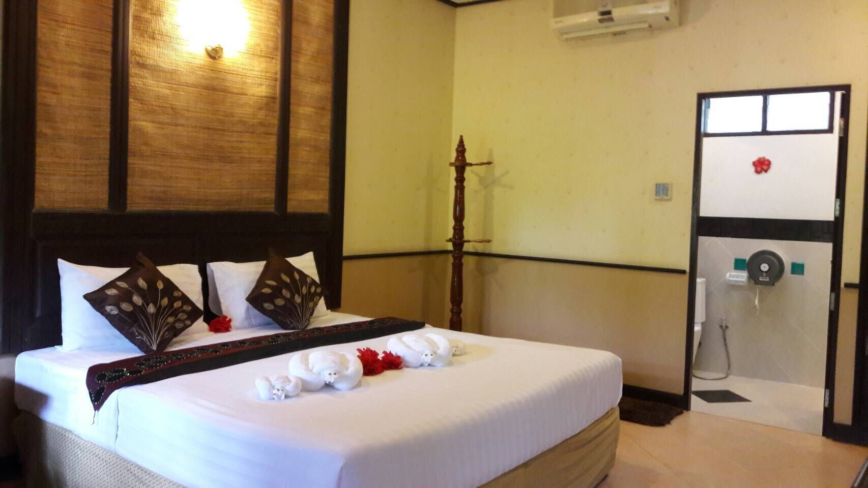 A hotel room with a neatly made bed, a wooden headboard, a large mirror, and a shower area with a towel rack.