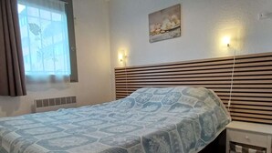 A bedroom with a bed, a nightstand, a wall-mounted light, and a window with blinds.