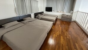 Ett hotellrum med tre sängar, en TV, ett fönster med gardiner och ett trägolv.