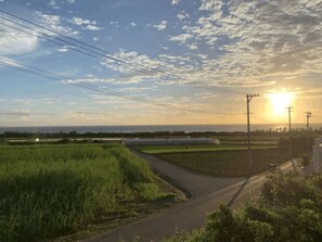 A rural landscape with a winding road, fields, and power lines under a partly cloudy sky with the sun setting. - JAM ClubHouse Resort (Yomitan)