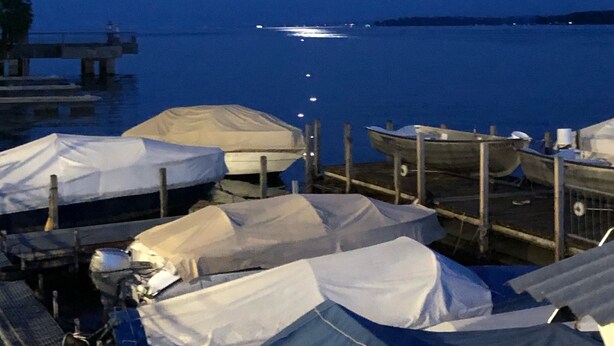 Un port de plaisance illuminé la nuit, où les bateaux sont recouverts de bâches blanches, sont amarrés et où l'eau est calme sous un ciel dégagé.