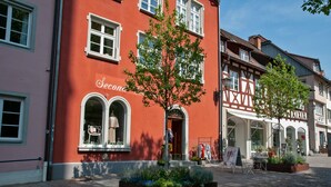 Une rue typique d’Europe, avec un bâtiment rouge doté de fenêtres en arc de cercle et d’une enseigne sur laquelle on peut lire « Second ».