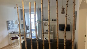 Un salon comprenant un canapé, une table à manger avec des chaises, un téléviseur et une fenêtre avec des rideaux.