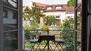 Un balcon avec une table et deux chaises, donnant sur un jardin et des immeubles d’habitation.