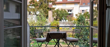 En balkon med et bord og to stole, der giver udsigt over en have og boligbygninger.