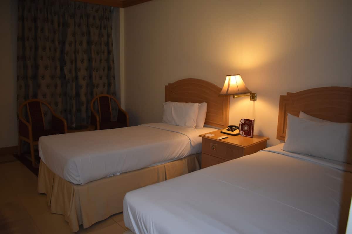 A hotel room with two single beds, a nightstand with a lamp, a telephone, and a small table.