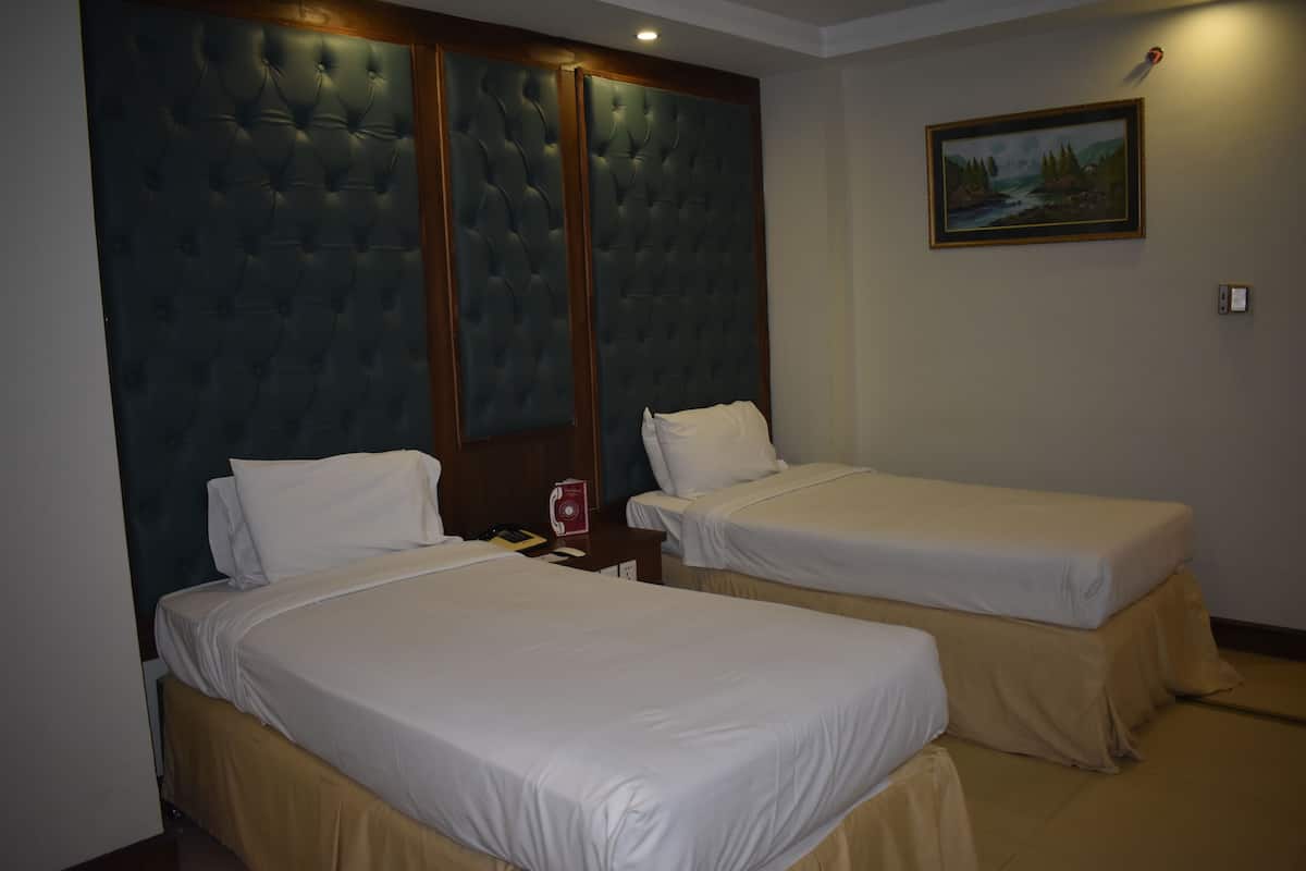A hotel room with two beds, a large tufted headboard, a painting on the wall, and a nightstand with a red object.