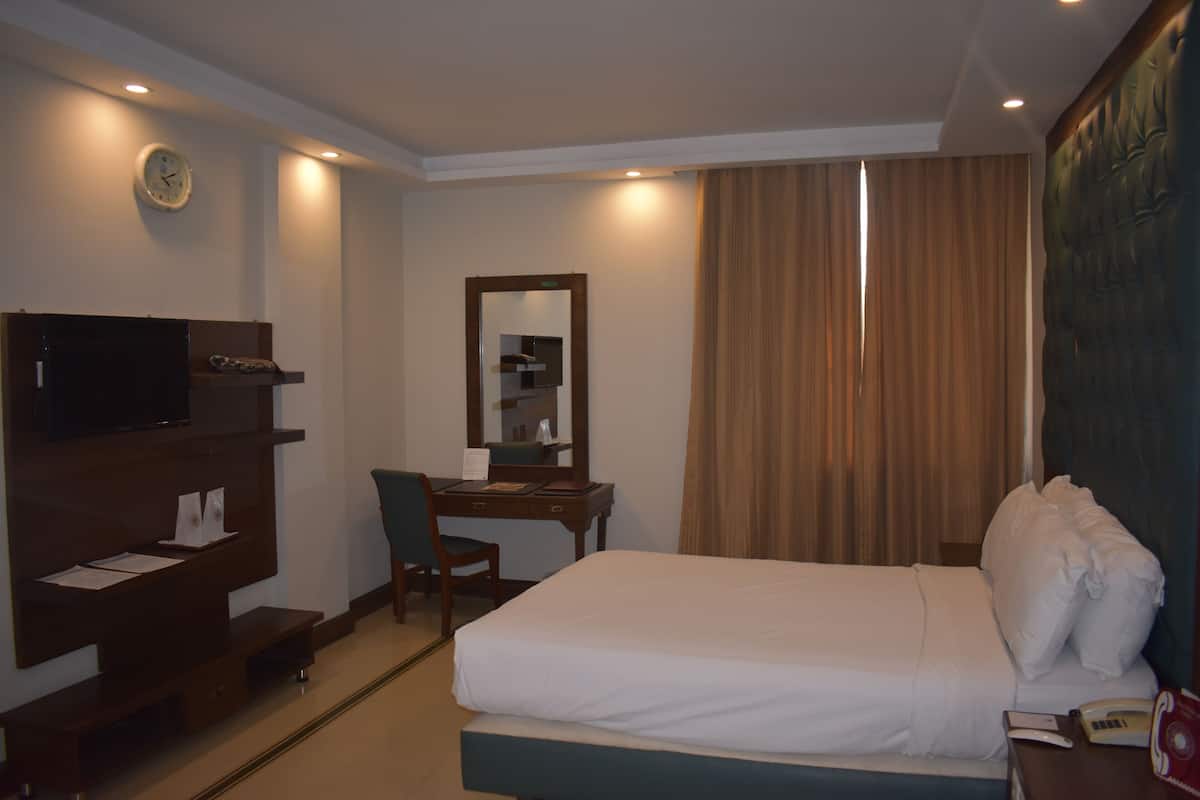 A hotel room with a bed, a desk, a chair, a television, and a clock on the wall.