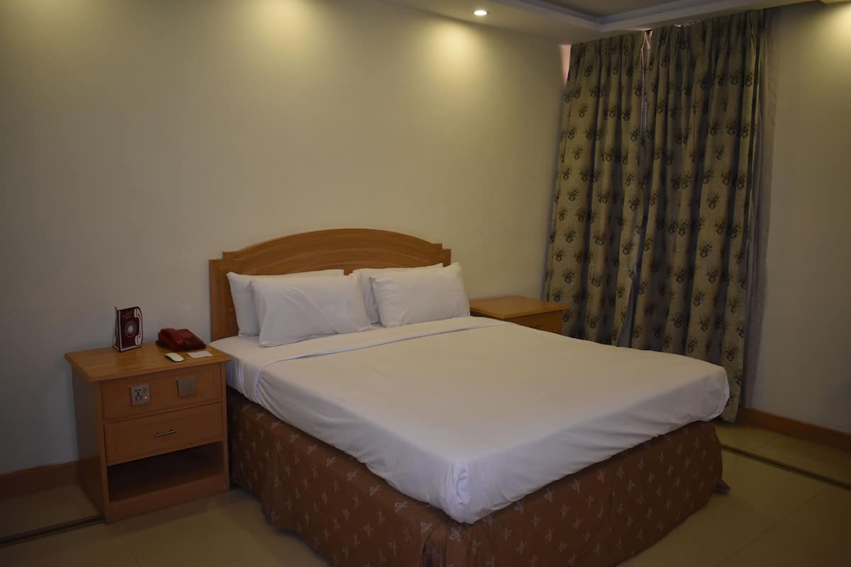 A neatly made bed with white linens, a wooden headboard, and a nightstand with a telephone and a book.