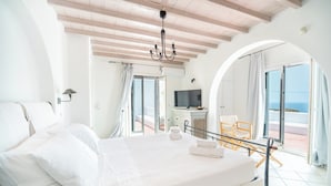 A bedroom with a large bed, a TV, and a view of the sea.