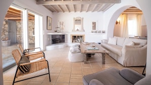 A spacious living room with a stone fireplace, a sofa, a coffee table, and wicker chairs.