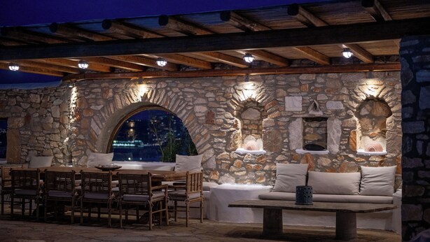 An outdoor patio with stone walls, wooden furniture, and built-in lighting.
