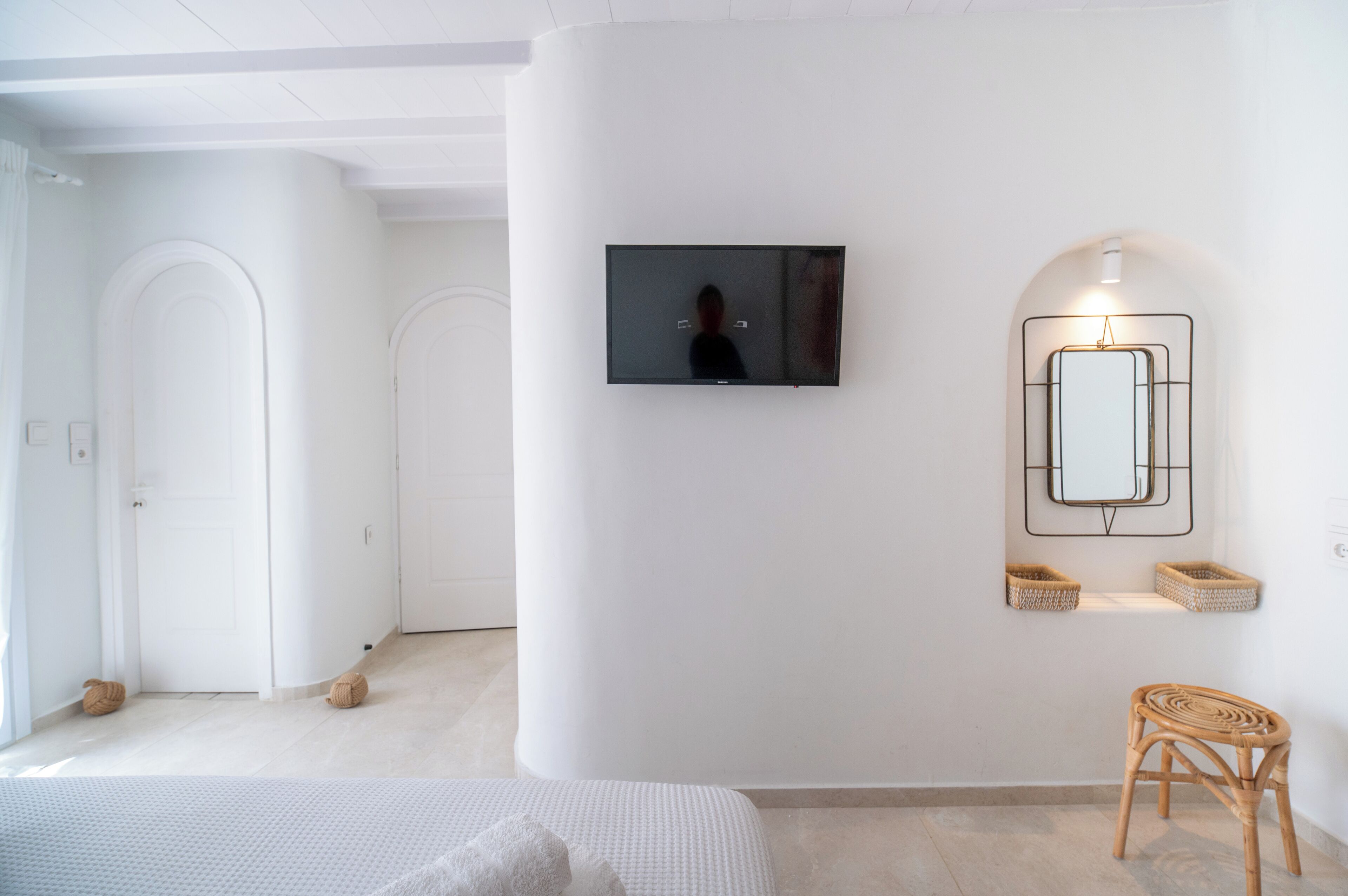 Ett modernt hotellrum med en platt-TV som är monterad på väggen, en stor spegel med en geometrisk ram och en fåtölj i rotting.