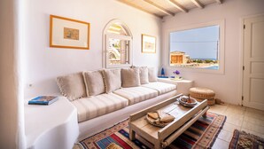 A cozy living room with a sofa, a coffee table, and a window with a view of the sea.