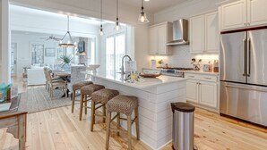 A modern kitchen with white cabinetry, stainless steel appliances, and a central island with bar stools. - Family-Friendly Home in Watercolor | Beach Club, *Golf Cart, Pool Access, Steps to Beach & Dining! (Santa Rosa Beach)
