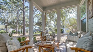 A covered porch with wooden furniture, a table, and a view of a residential area. - Family-Friendly Home in Watercolor | Beach Club, *Golf Cart, Pool Access, Steps to Beach & Dining! (Santa Rosa Beach)