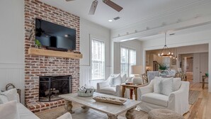 A spacious living room with a brick fireplace, white furniture, and a large TV. - Family-Friendly Home in Watercolor | Beach Club, *Golf Cart, Pool Access, Steps to Beach & Dining! (Santa Rosa Beach)